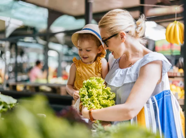 Une femme achète de la laitue avec son enfant au marché aux légumes